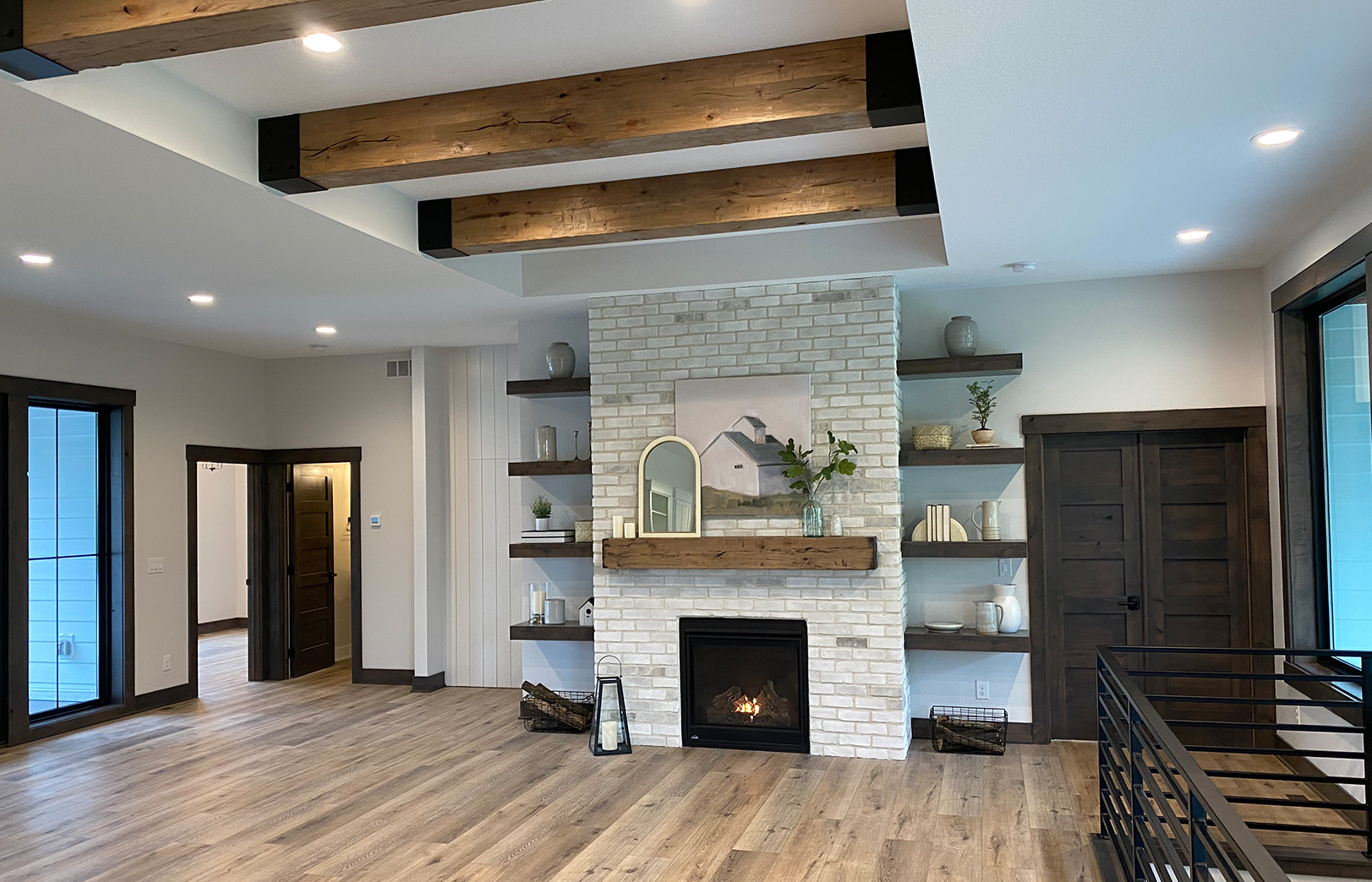 from kitchen sink overlooking greatroom with large beams overhead, fireplace and black railing leading downstairs