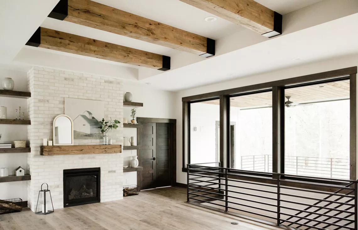 overlooking greatroom with large beams overhead, fireplace and black railing leading downstairs