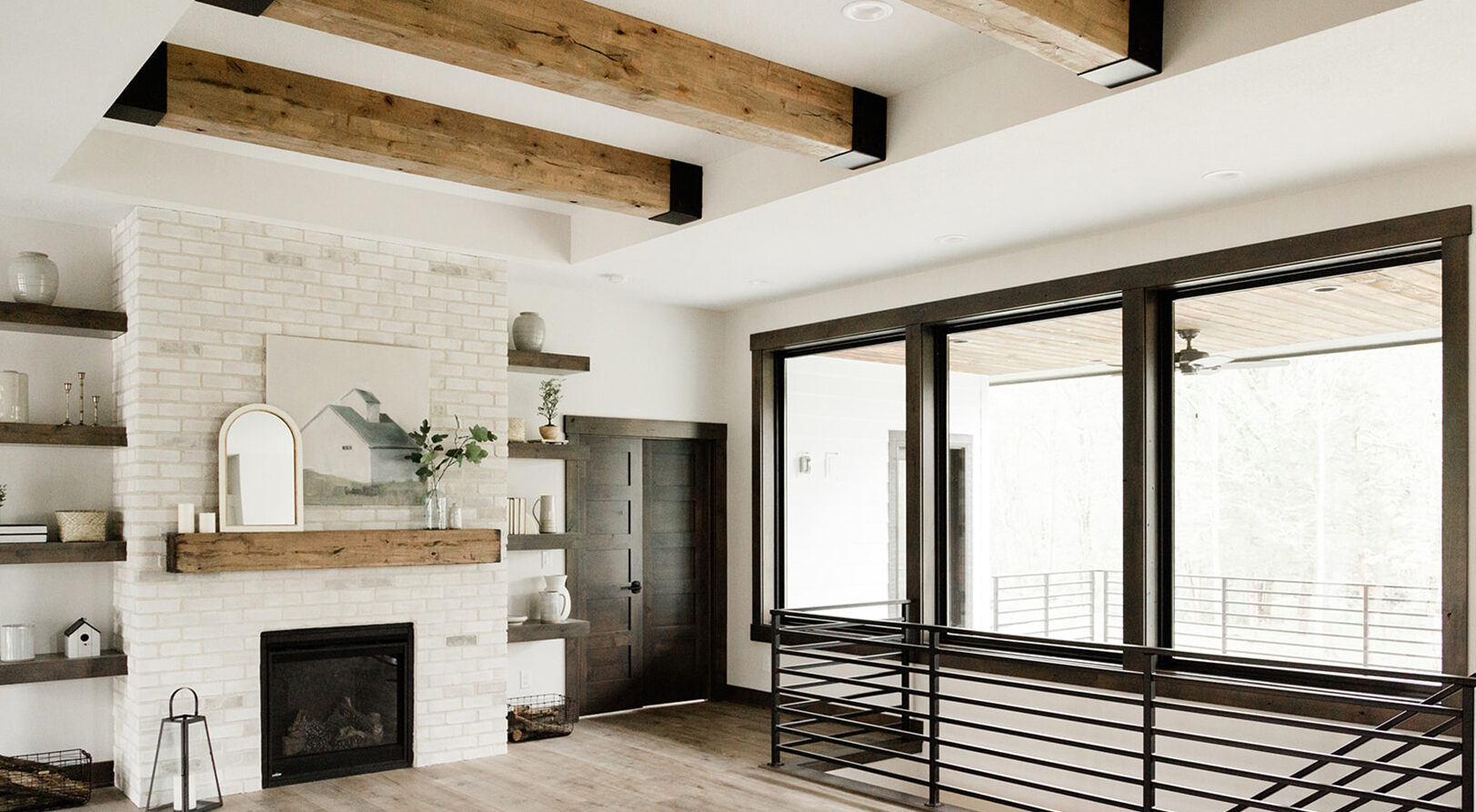 overlooking greatroom with large beams overhead, fireplace and black railing leading downstairs