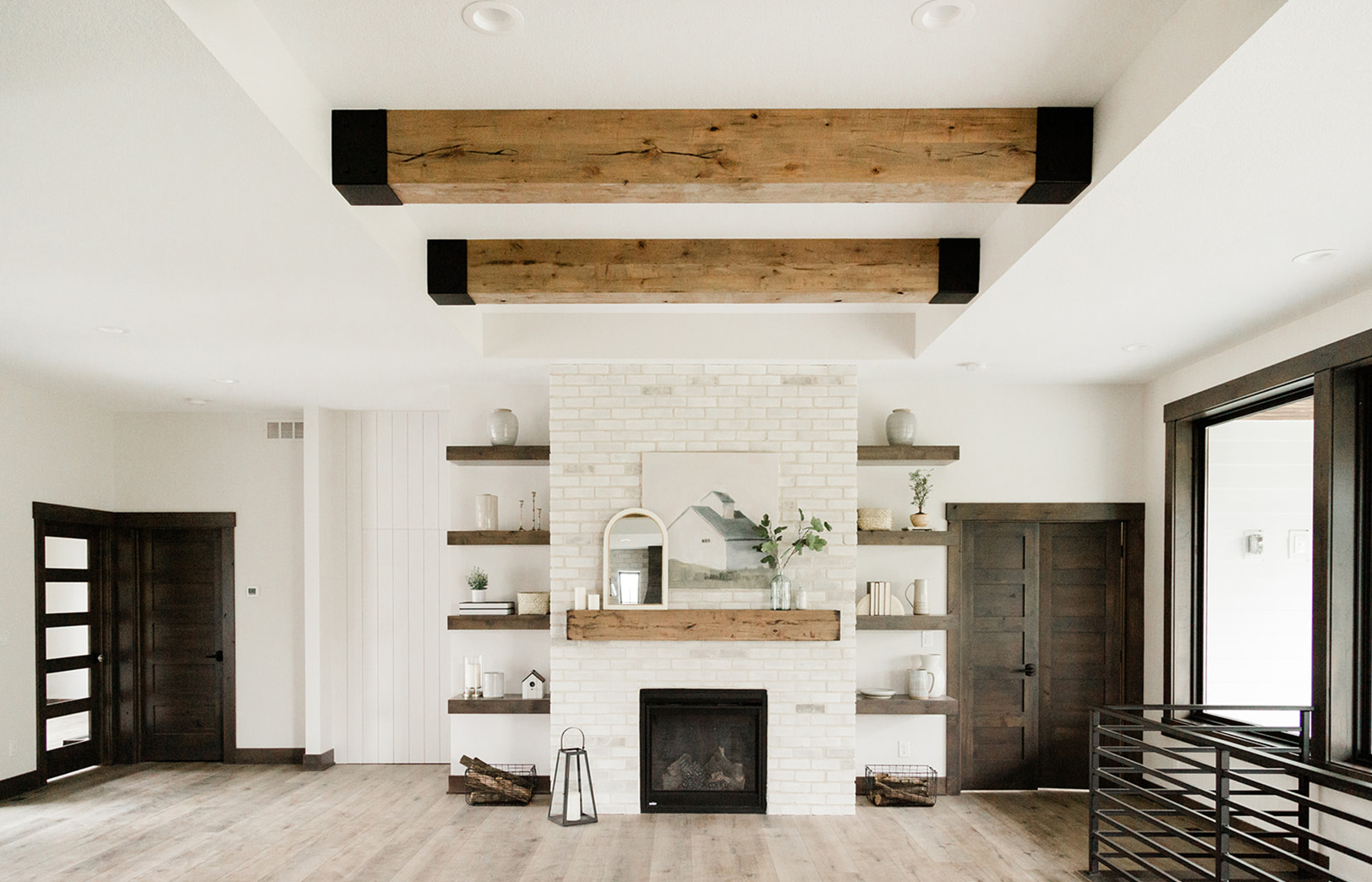 from kitchen sink overlooking greatroom with large beams overhead, fireplace and black railing leading downstairs
