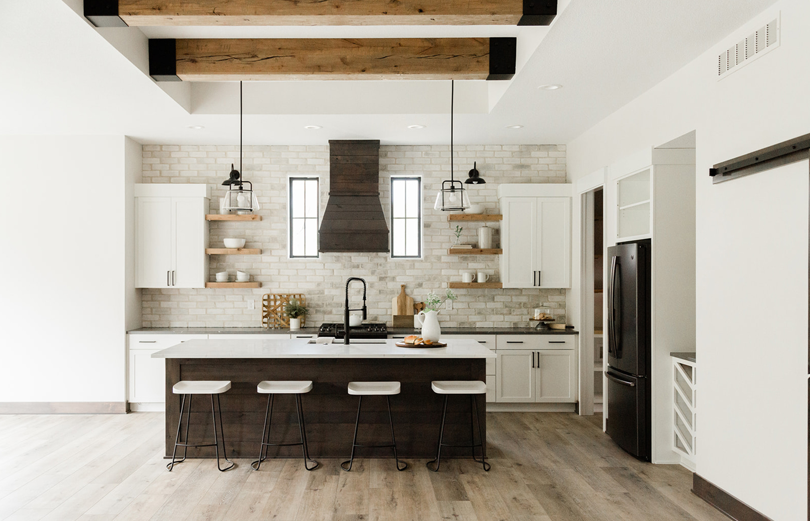 large beams over kitchen island that has four stools and stone accent wall with large wooden oven hood