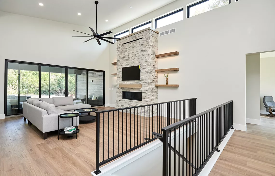 large open concept living area with light plank flooring, stacked stone fireplace and double sliding glass doors