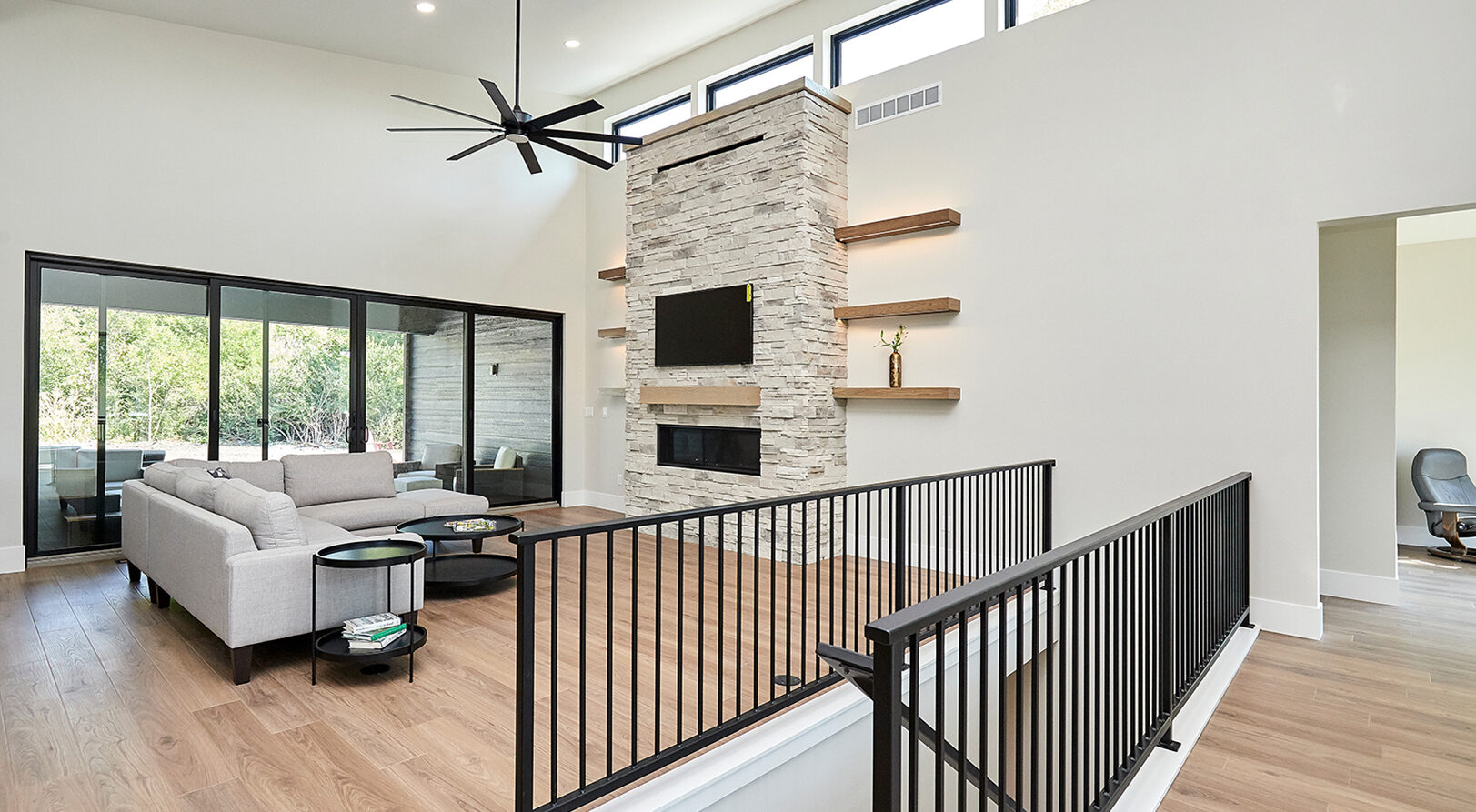 large open concept living area with light plank flooring, stacked stone fireplace and double sliding glass doors