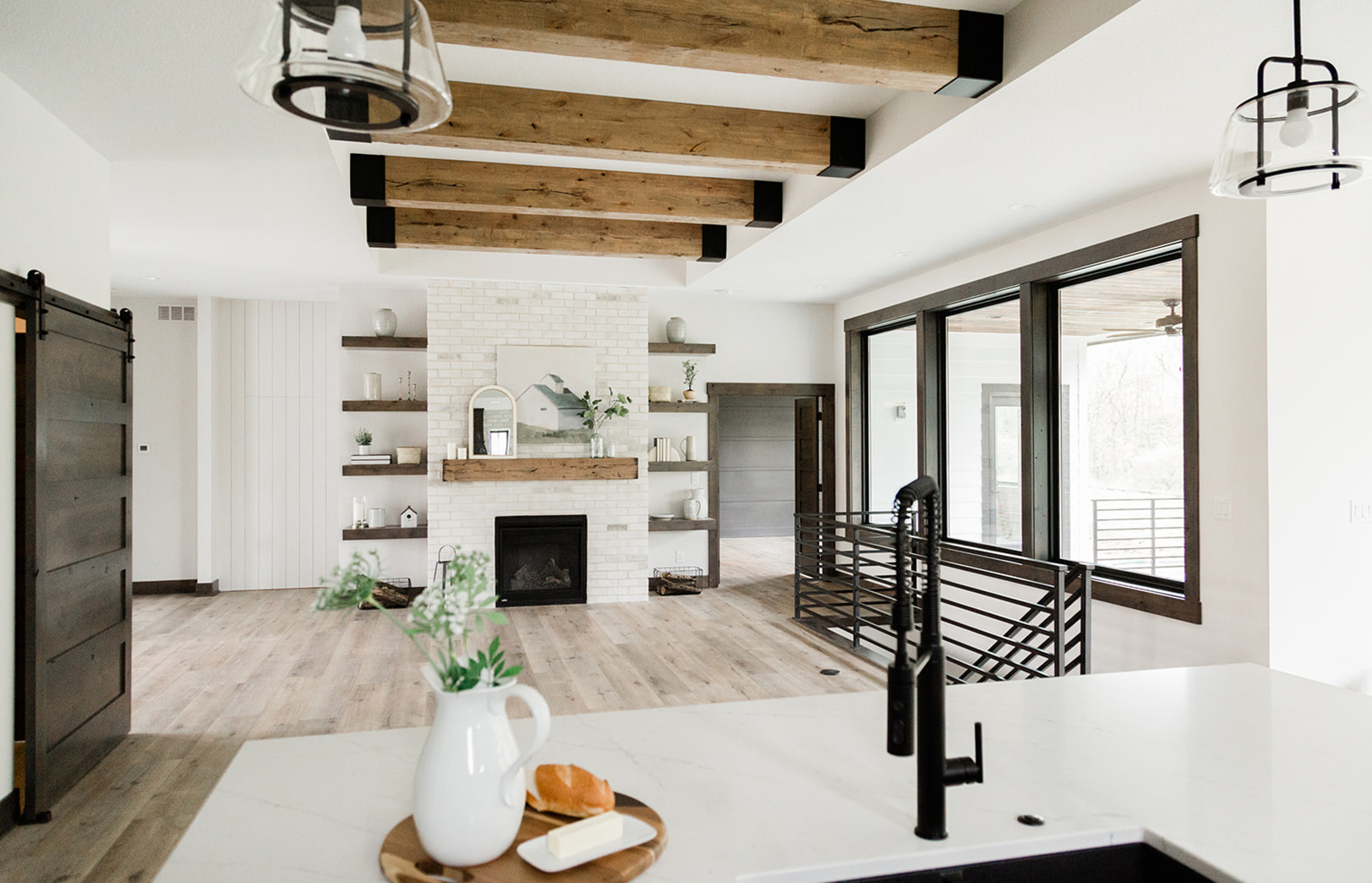 from kitchen sink overlooking greatroom with large beams overhead, fireplace and black railing leading downstairs