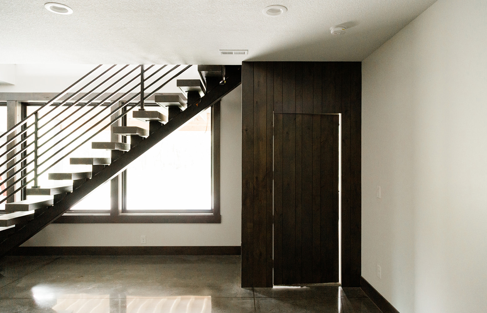 stairs with metal railing and wooden accent wall into adjacent room