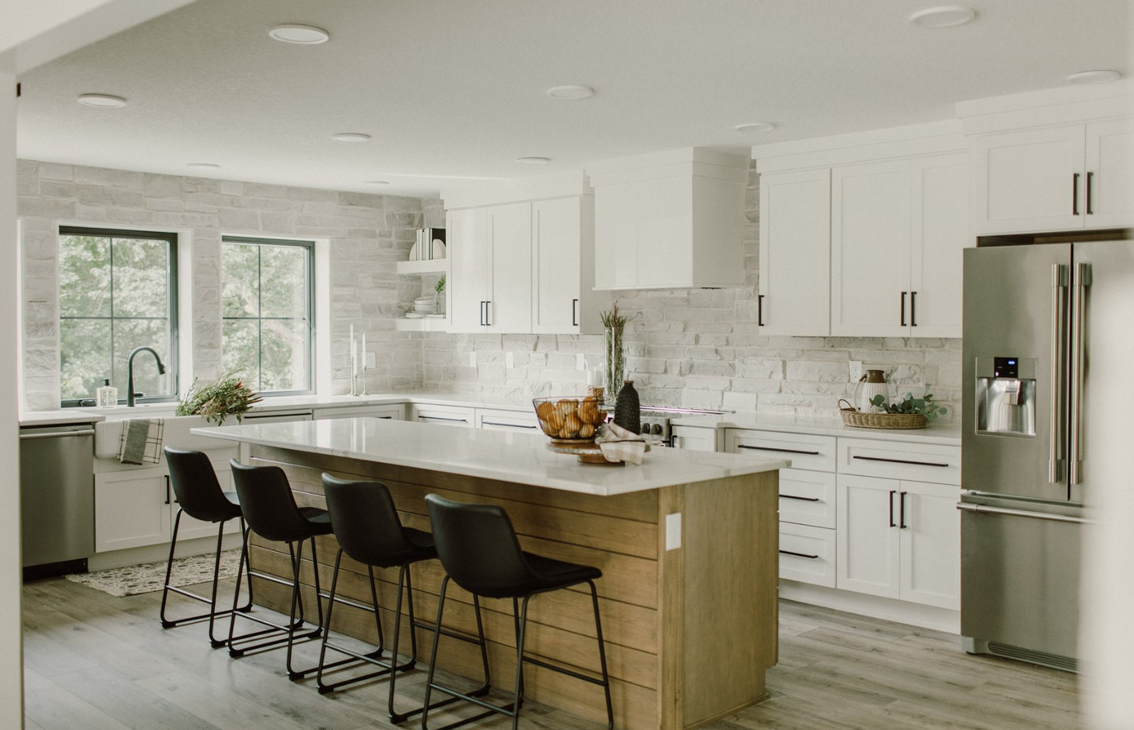 renovated kitchen with white cabinets, white counter and tan wood island with black chairs