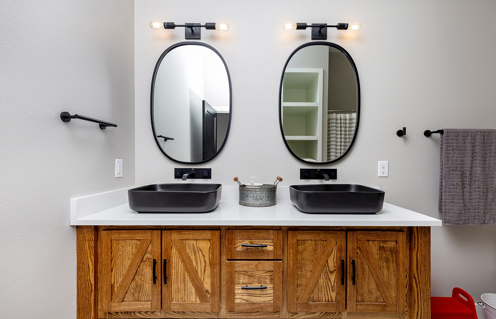 Bathroom with two mirrors over black sinks, white counter and wood cabinets