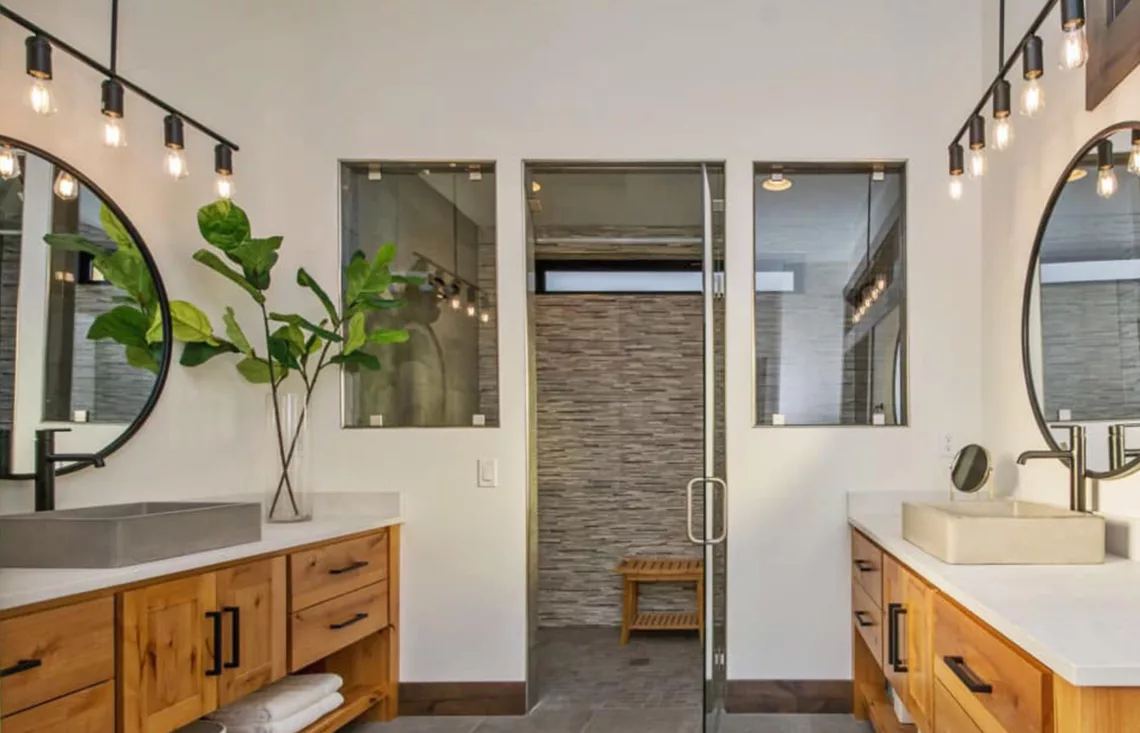 mirrored vanities with stone sinks circle mirrors hanging lights looking into large tiled shower room