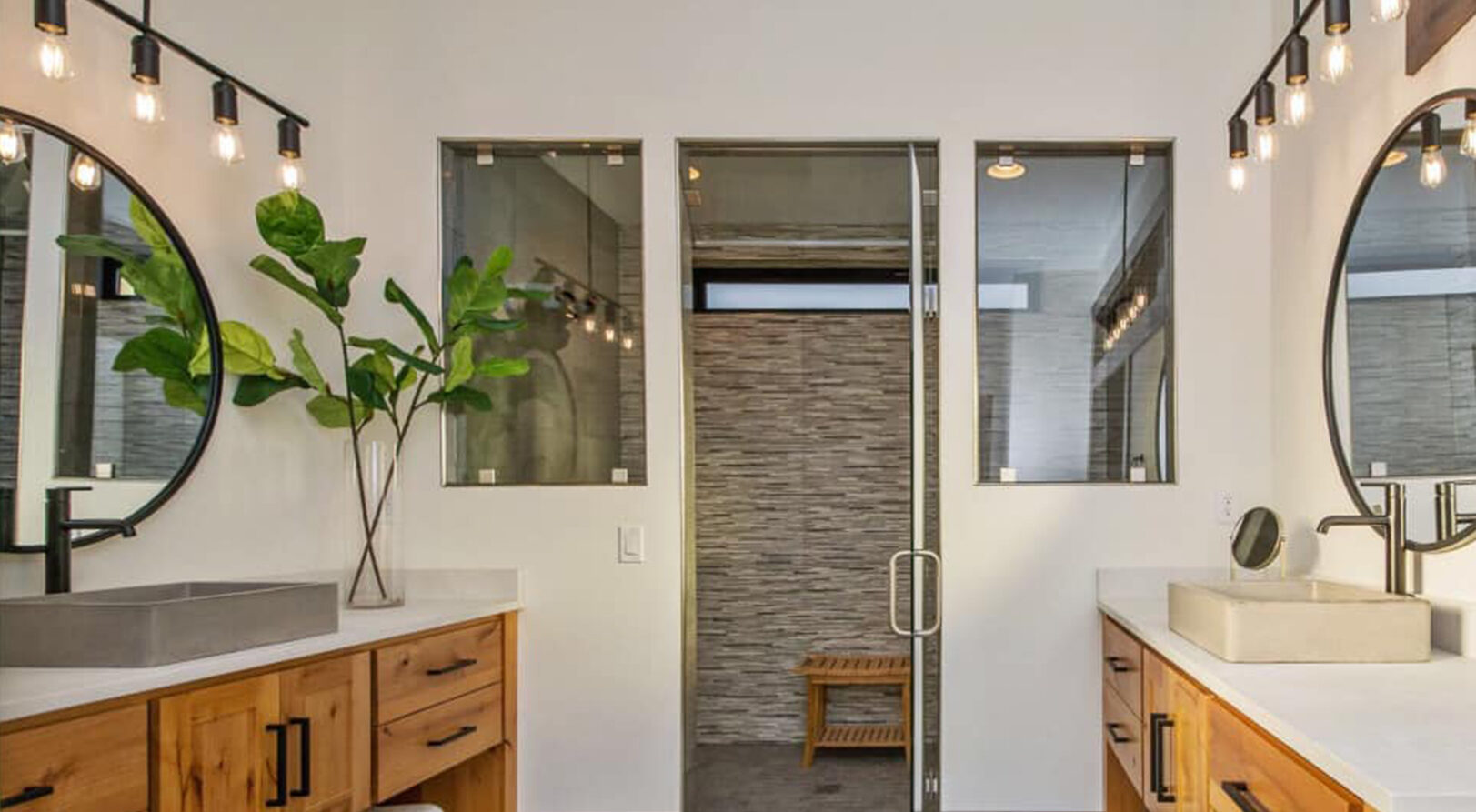 mirrored vanities with stone sinks circle mirrors hanging lights looking into large tiled shower room