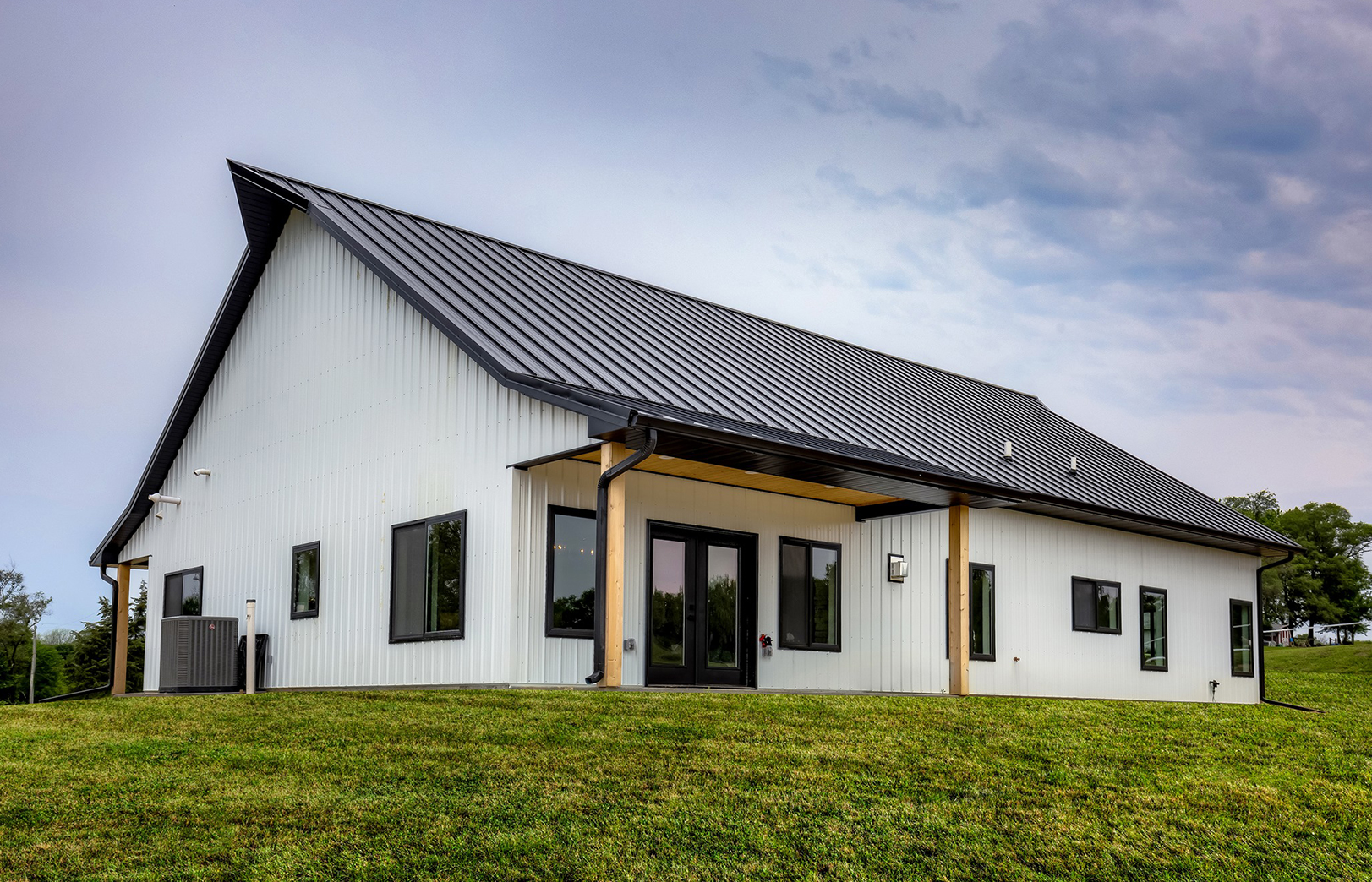 Exterior metal white home with black roof and wood beams