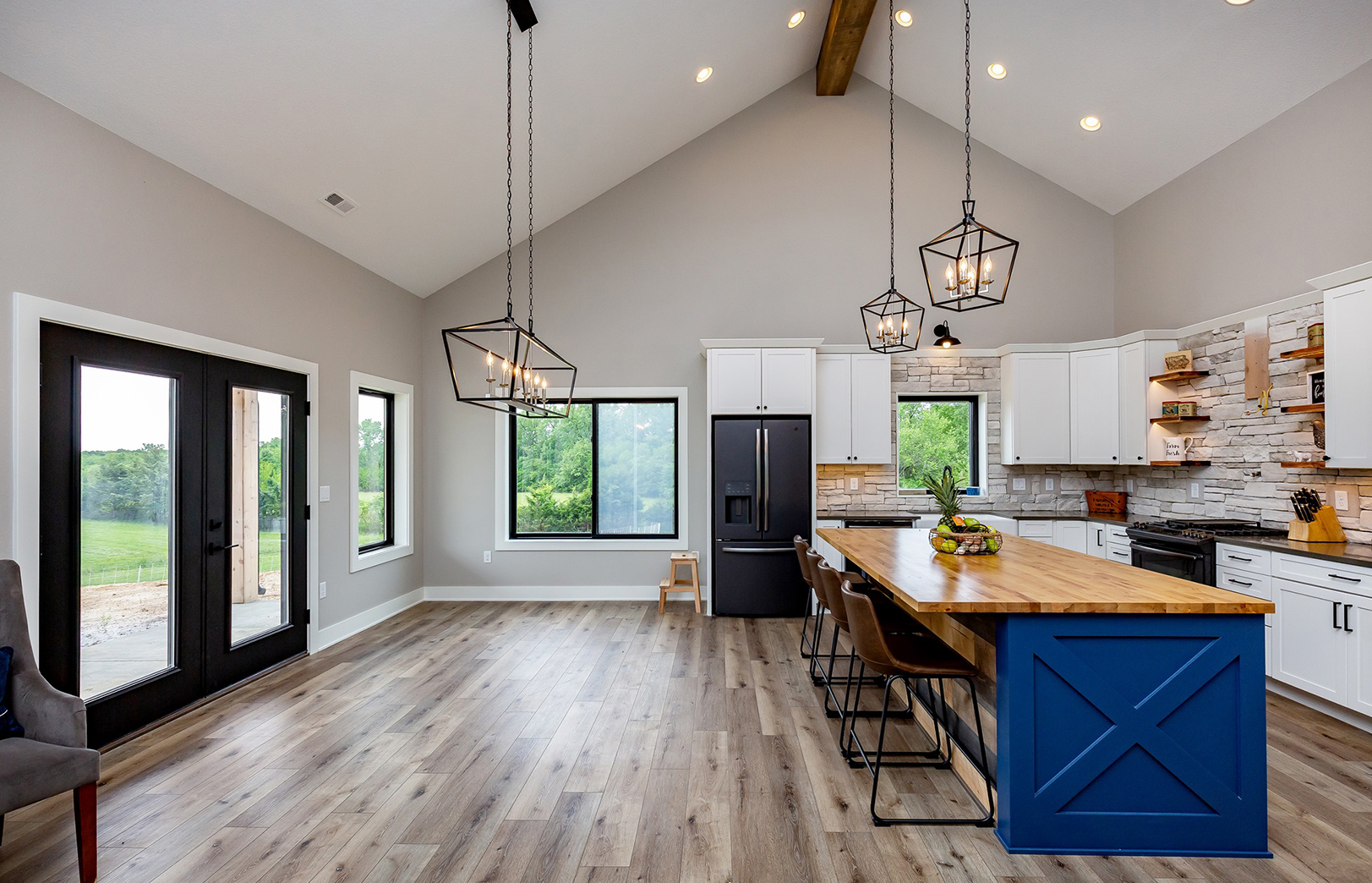kitchen with black refrigerator, white cabinets, wood island with four chairs and two hanging light fixtures, blue accent wood