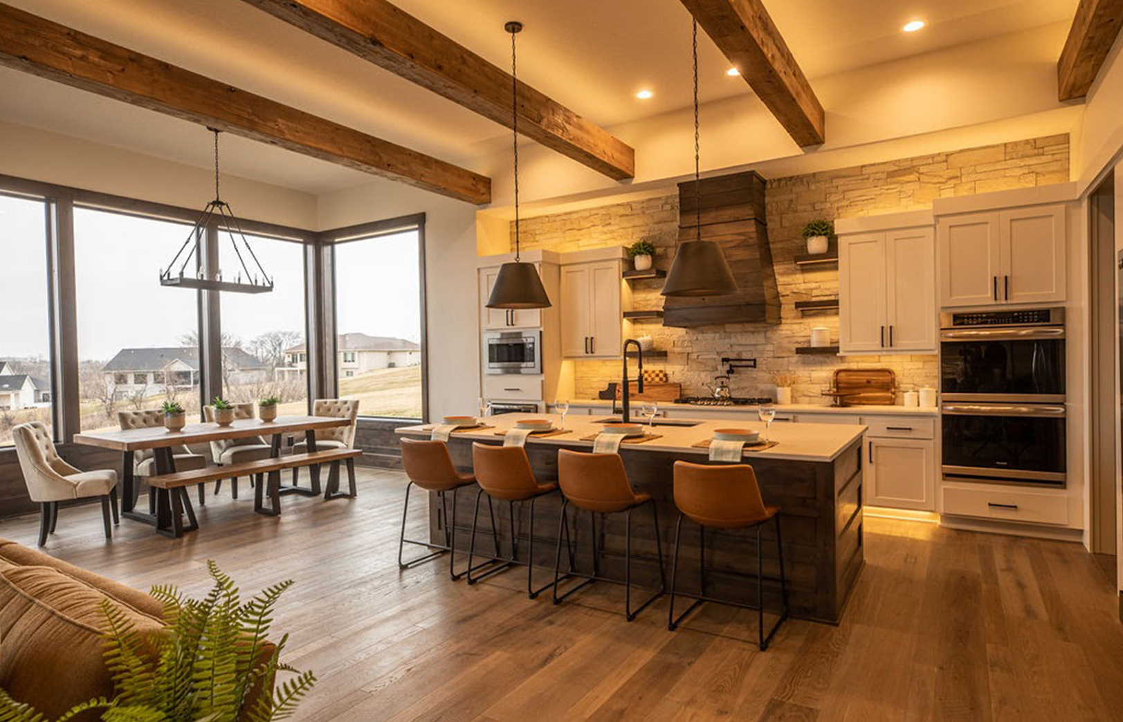entire kitchen area into breakfast nook with four chairs at the counter and large kitchen table and large wooden beams overhead