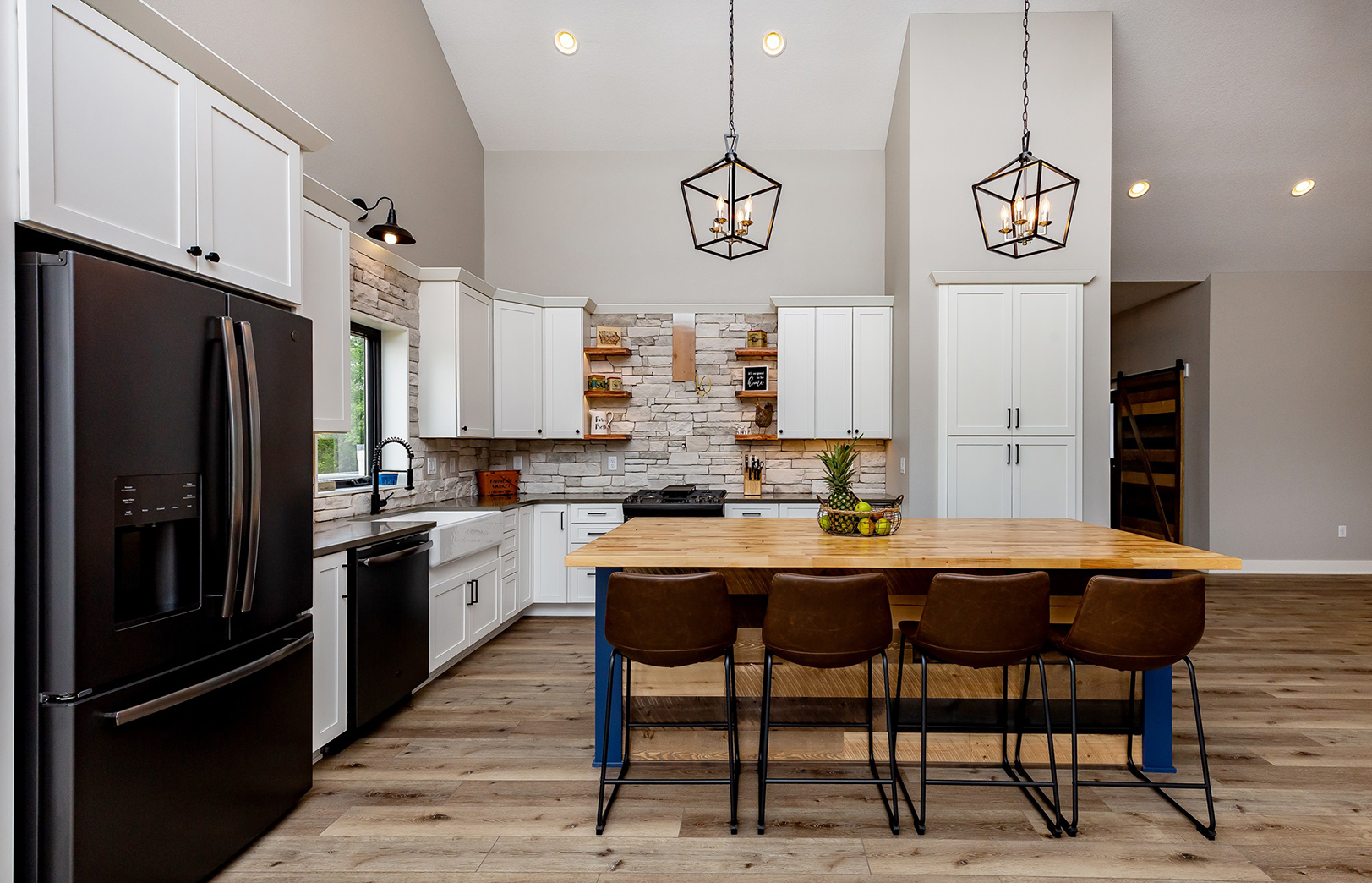kitchen with black refrigerator, white cabinets, wood island with four chairs and two hanging light fixtures
