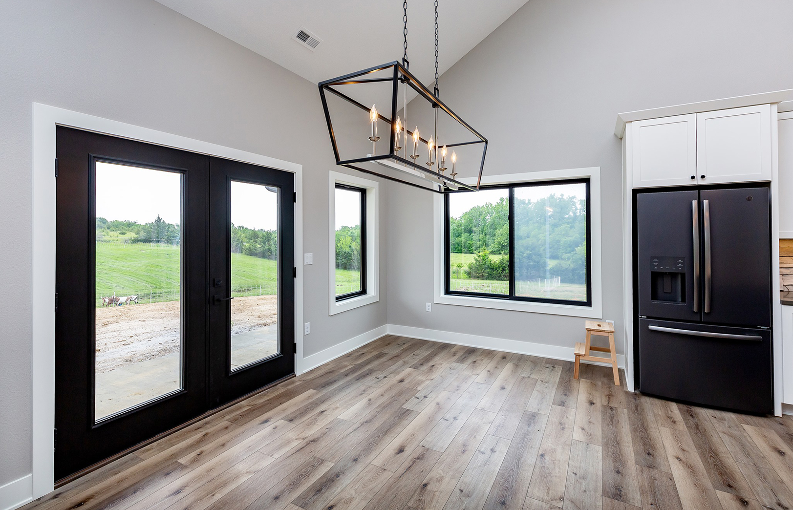 Wood floors, black refrigerator glass doors leading outside and large hanging light fixture