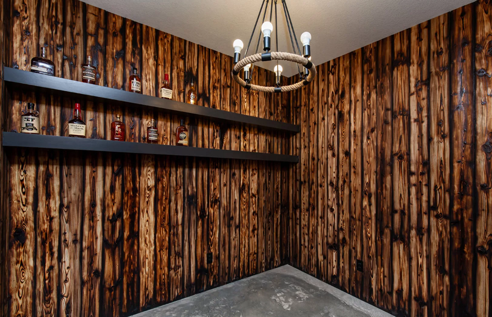 rustic burnt wood paneling with rope hanging light fixture and shelves with liquor bottles