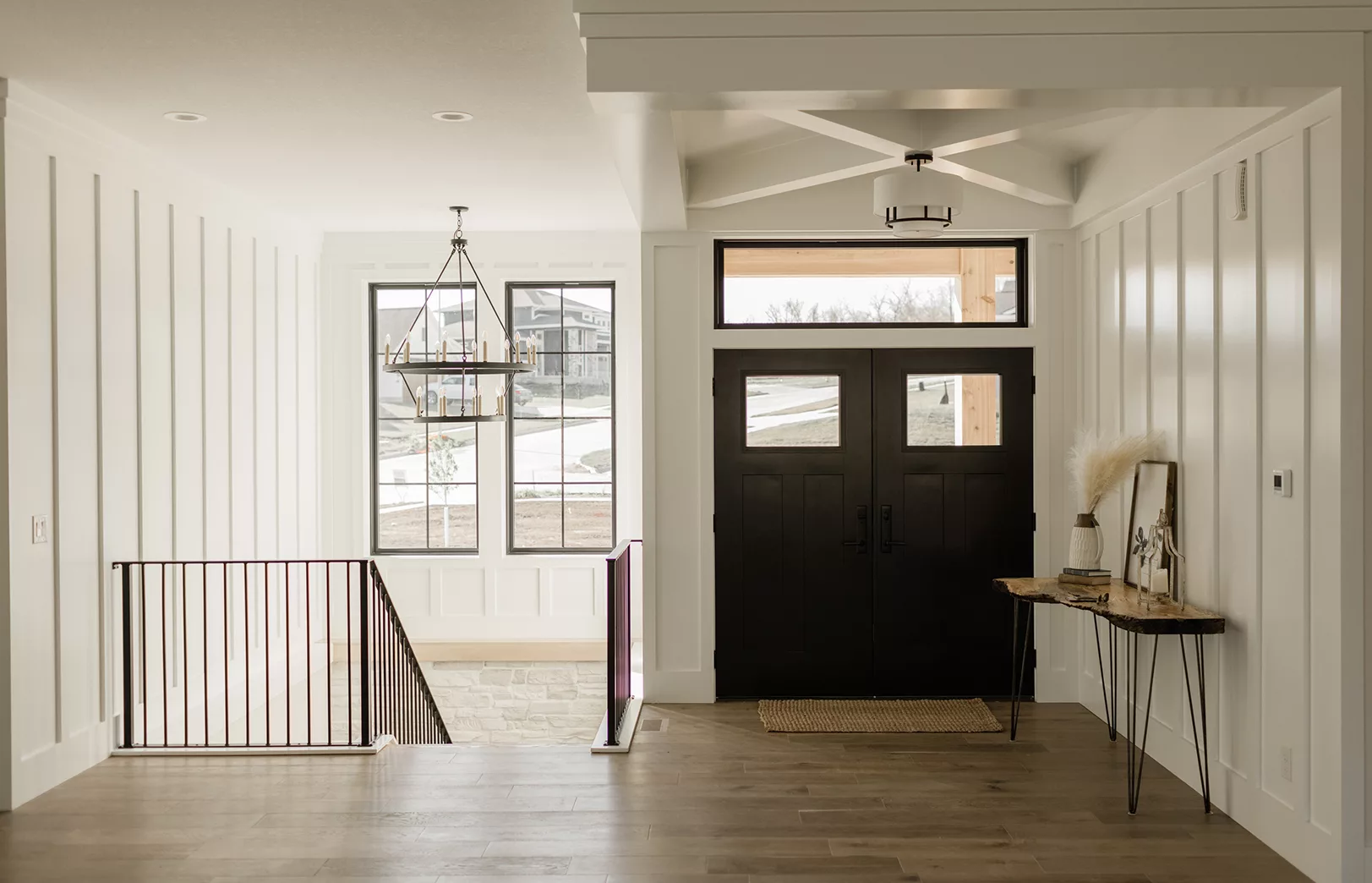 entryway with black double doors and chandelier over stairs leading down with wrought iron details