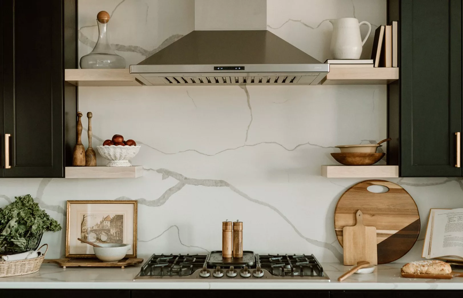 kitchen cook area with large marble accent wall, modern range hood and natural wood floating shelves