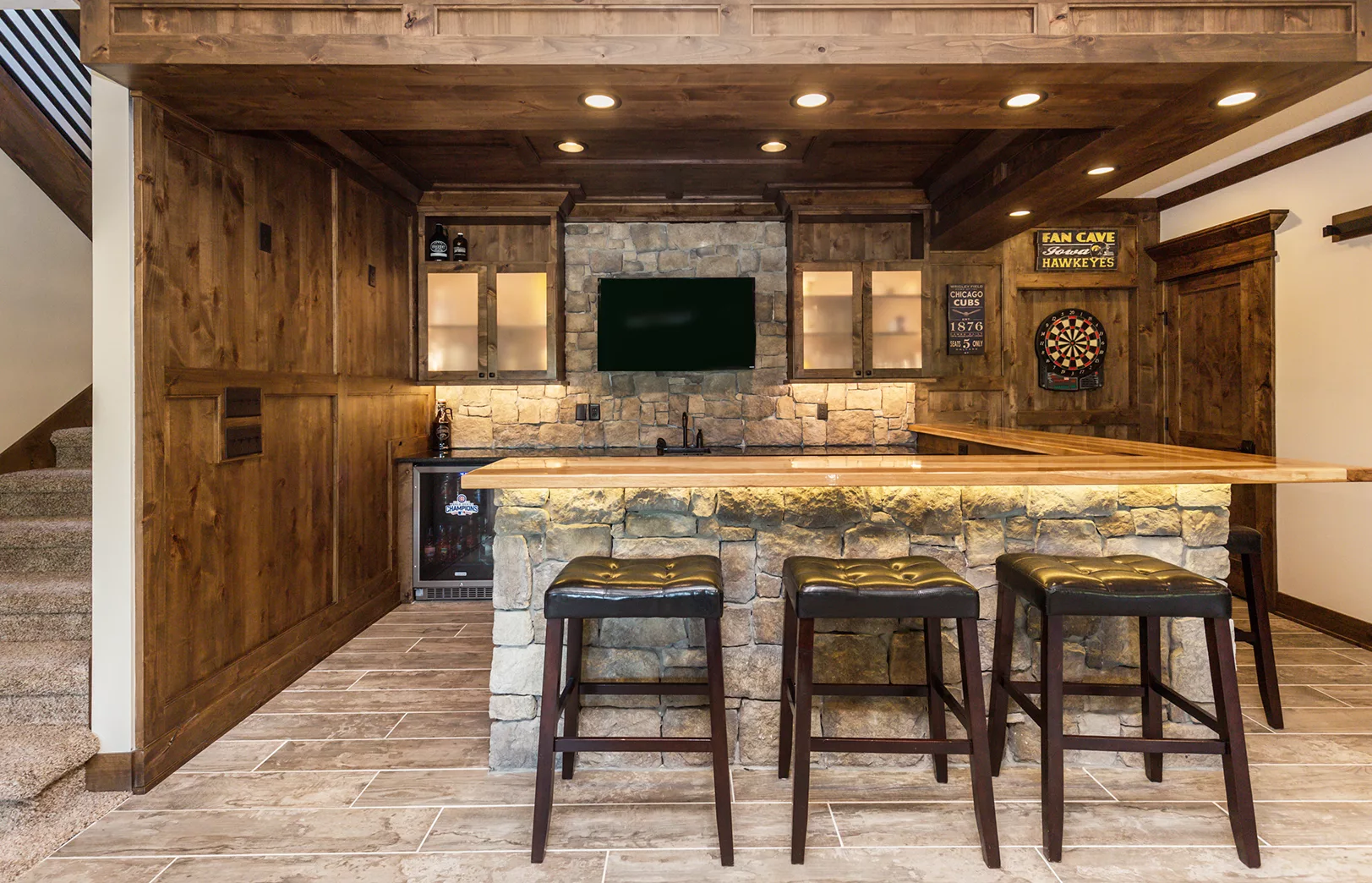 large bar area with three stools in front of stacked stone and rustic wood