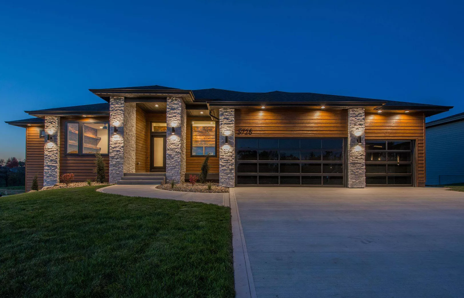 lighted home exterior with stained wood siding and stacked stone pillars