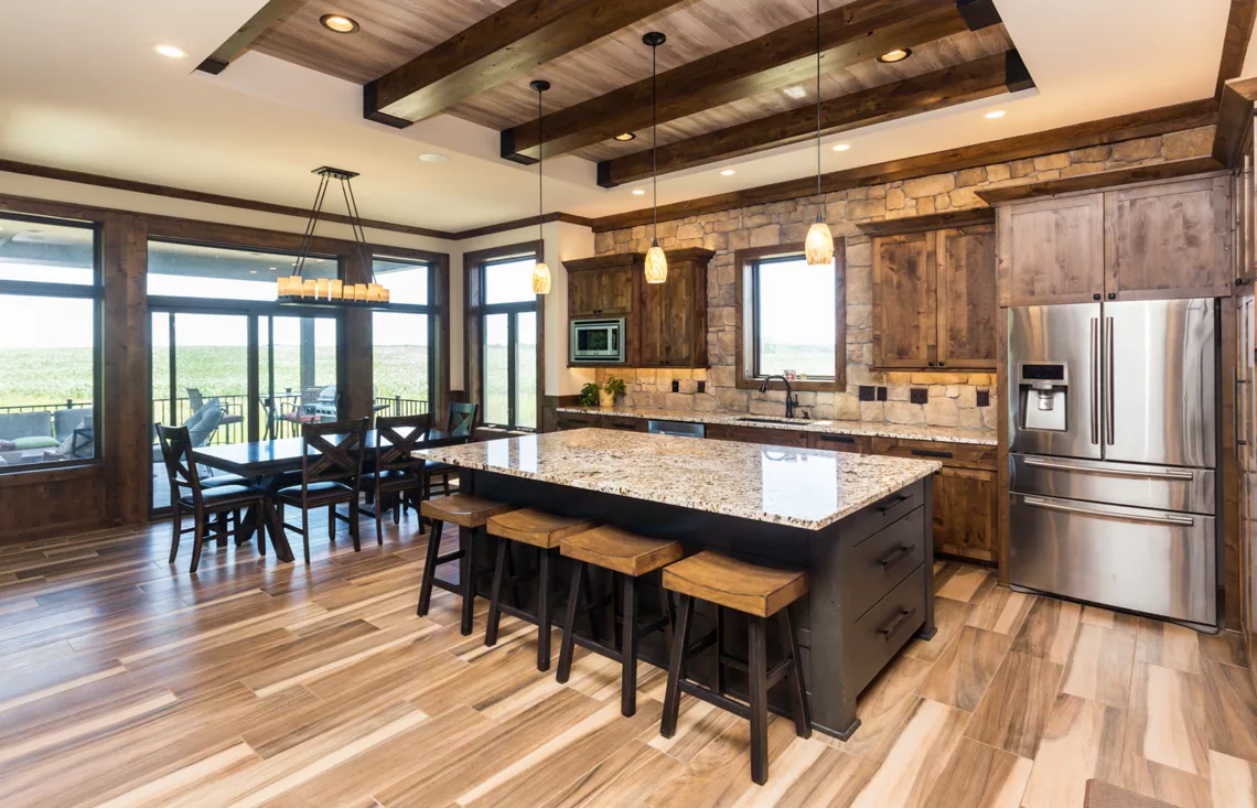 eat-in kitchen with large island, stacked stone accent wall and rustic wood beams and cabinets, large windows surrounding