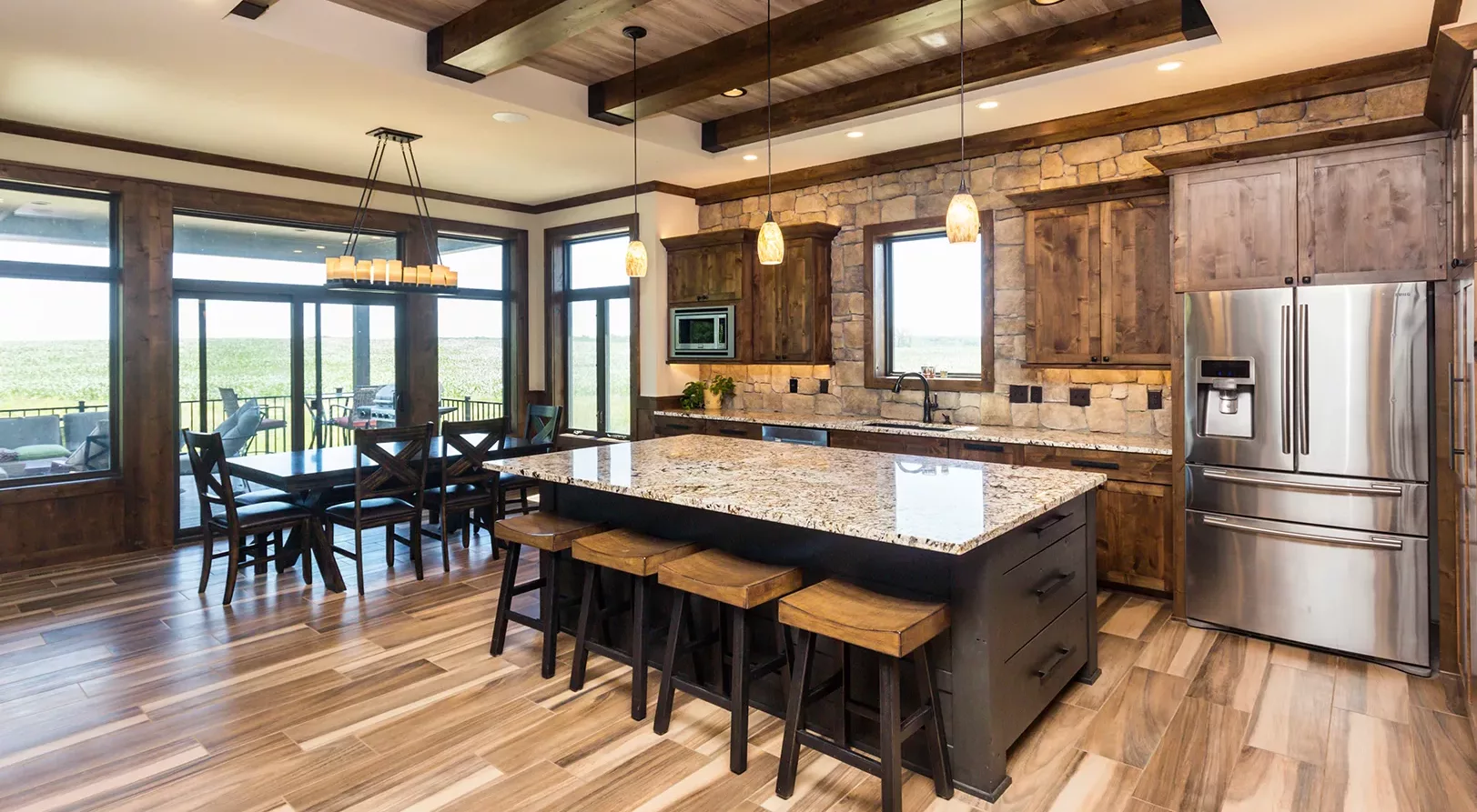 eat-in kitchen with large island, stacked stone accent wall and rustic wood beams and cabinets, large windows surrounding