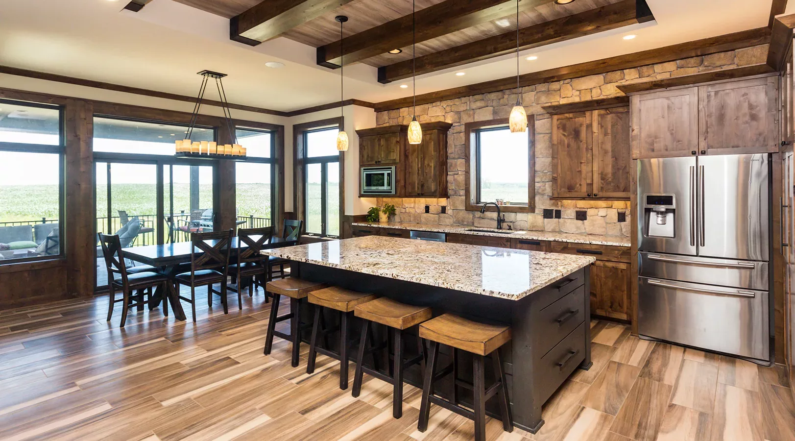 eat-in kitchen with large island, stacked stone accent wall and rustic wood beams and cabinets, large windows surrounding