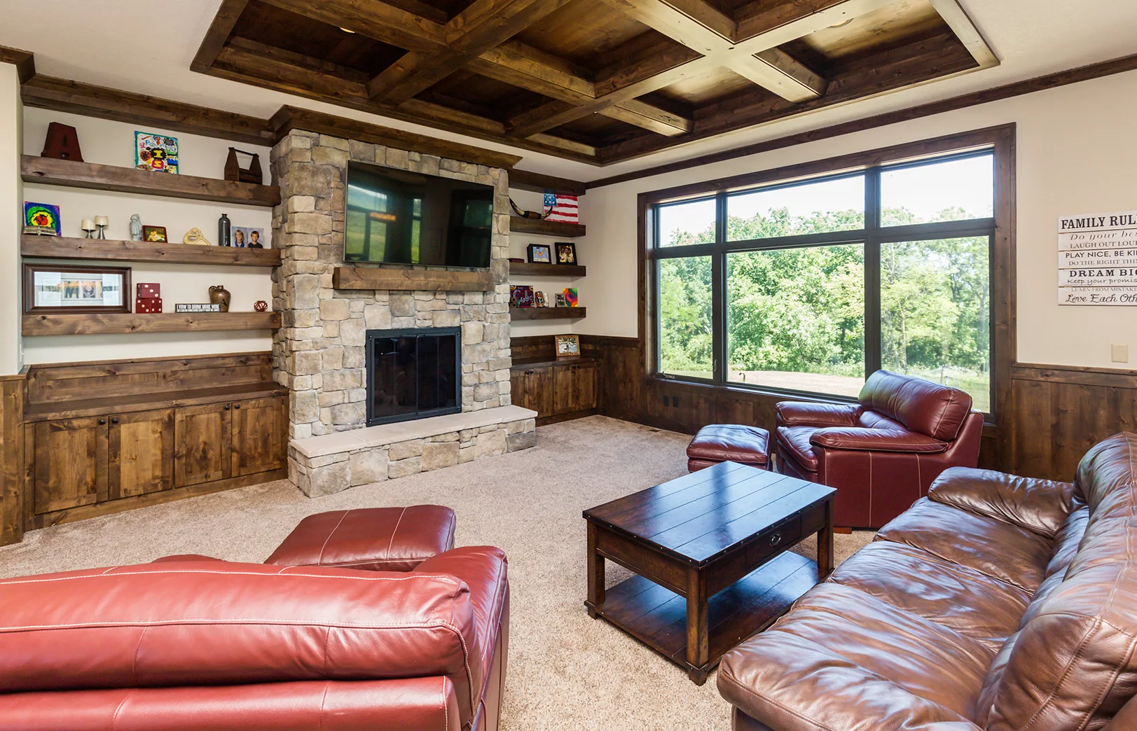 open living area with large stacked stone fireplace, rustic wood cabinets, open floating shelves, large windows and wood ceiling